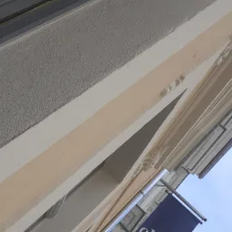 Fragment elewacji budynku z dekoracyjnymi elementami sztukaterii, świeżo pomalowany w odcieniach szarości, bieli i beżu, widok z dołu na tle błękitnego nieba.