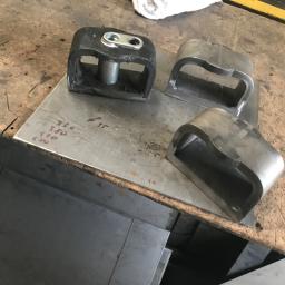 Auto-remont Łukasz Wójcik - Czarne i srebrne metalowe elementy obróbki blacharskiej leżące na płycie z odręcznymi notatkami, widoczne arkusze blachy w tle.