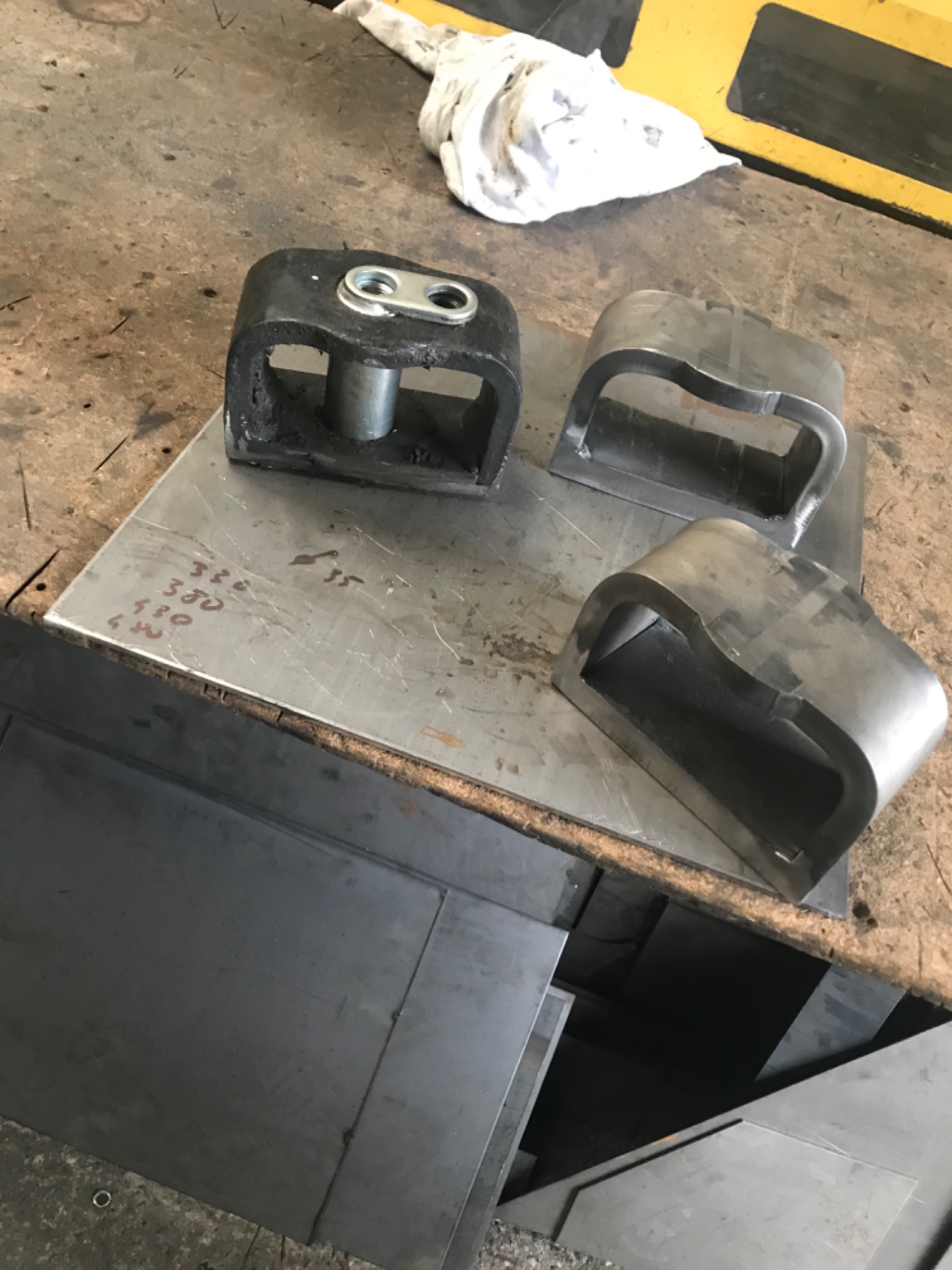 Czarne i srebrne metalowe elementy obróbki blacharskiej leżące na płycie z odręcznymi notatkami, widoczne arkusze blachy w tle.