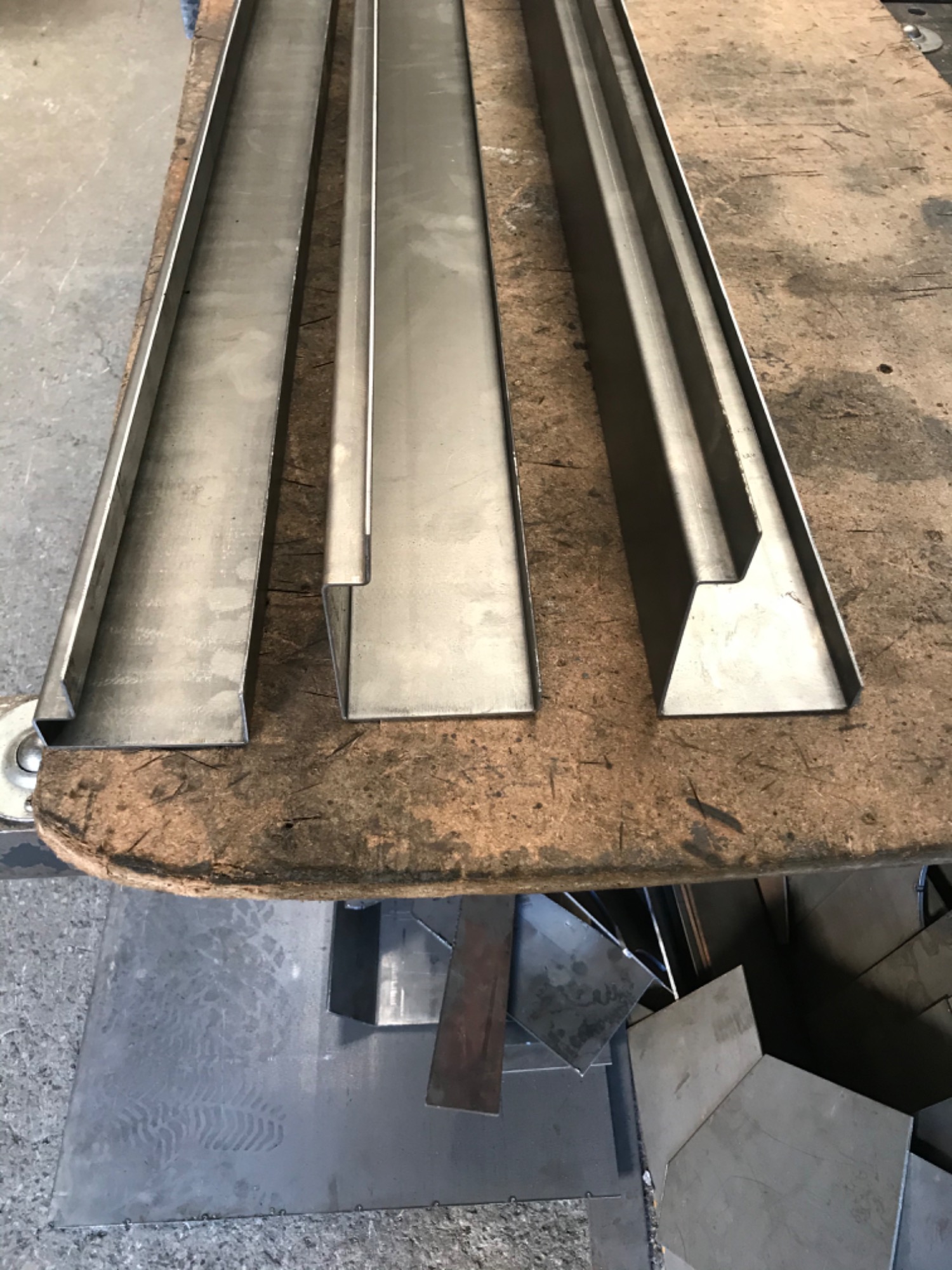 Przygotowane do montażu, surowe, metalowe elementy rynnowe o różnych profilach leżące na roboczym stole z widocznymi śladami użytkowania.