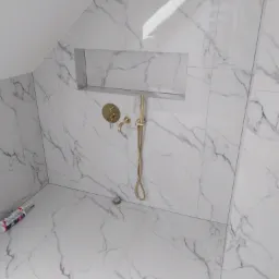 Wykończona łazienka na poddaszu z białymi płytkami imitującymi marmur, złotą armaturą i wnęką w ścianie.