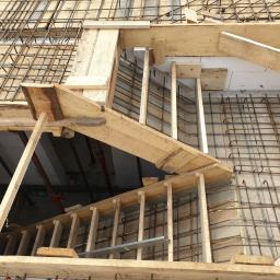 firma budowlana Kania - Zbrojenie schodów z drewnianym szalunkiem w trakcie budowy domu, widoczne pręty stalowe i elementy konstrukcyjne.