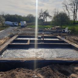 firma budowlana Kania - Zalane betonem szalunki fundamentowe z hydroizolacją, widoczne przygotowane podłoże, na dalszym planie betoniarka i samochód dostawczy.