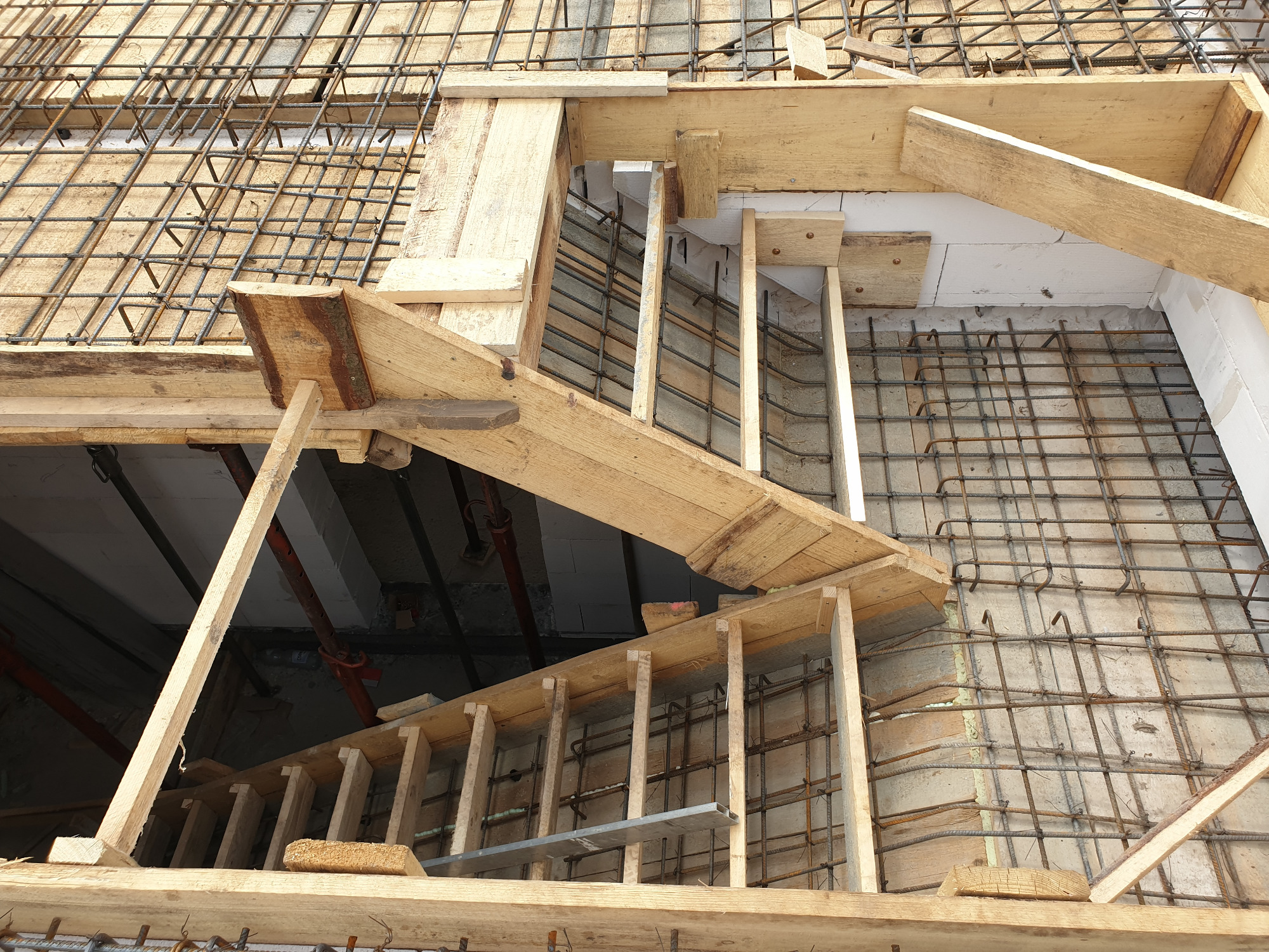 Zbrojenie schodów z drewnianym szalunkiem w trakcie budowy domu, widoczne pręty stalowe i elementy konstrukcyjne.