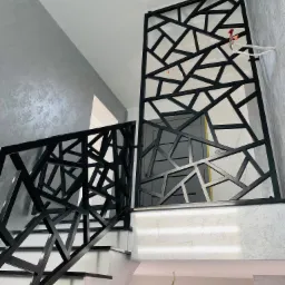 Nowoczesna, czarna balustrada schodowa z geometrycznym wzorem, widoczne niedokończone podłączenia elektryczne w tle.