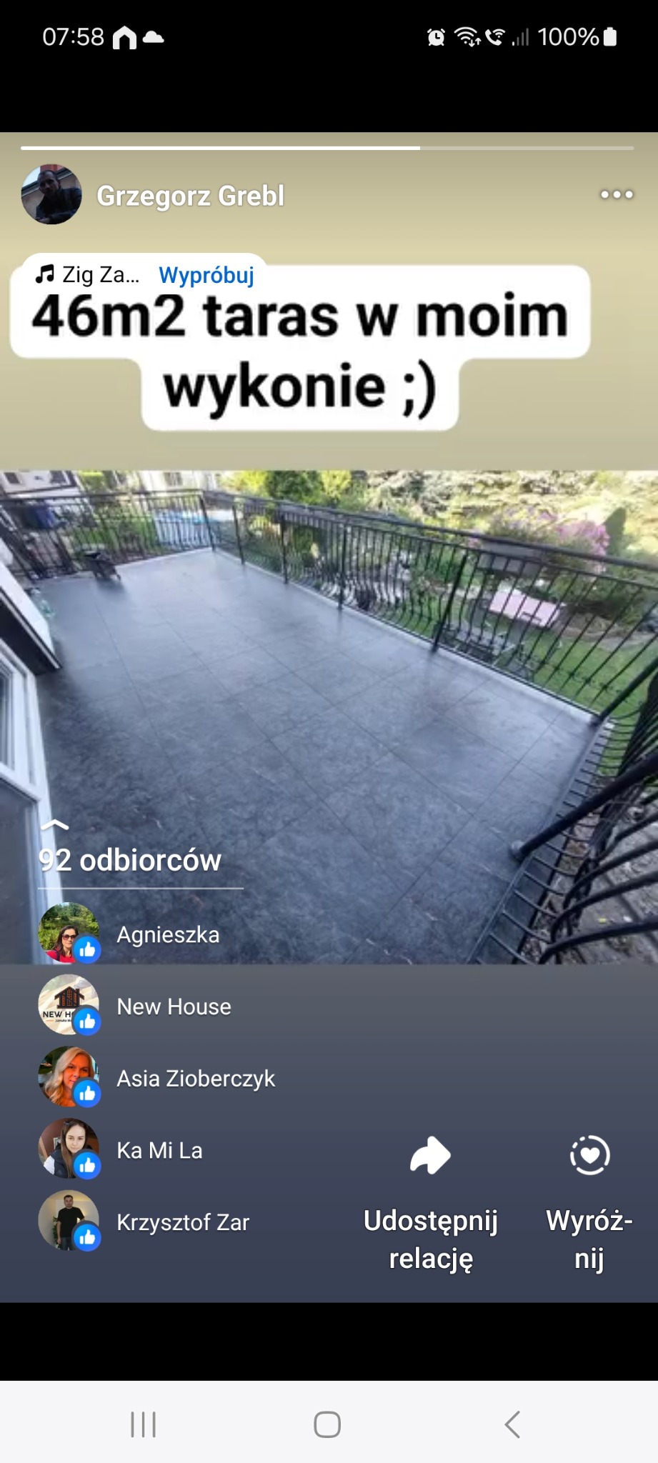 Wykończony taras o powierzchni 46m2 z ciemnymi, kwadratowymi płytkami i czarną, metalową balustradą. Tło z zielenią drzew. Widok z góry.