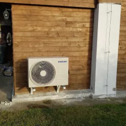 Klimatyzator Samsung zamontowany na drewnianej ścianie budynku, widoczne okablowanie i fragment trawnika.