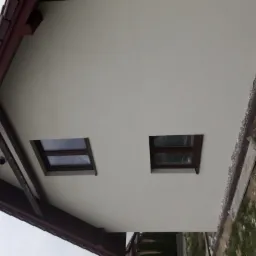 Ocieplona elewacja domu jednorodzinnego z dwoma oknami, widoczne rusztowanie i dach z brązową dachówką.