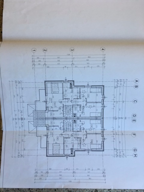 Plan architektoniczny dwukondygnacyjnego domu z wymiarami, widok z góry, wydruk na papierze leżącym na blacie.