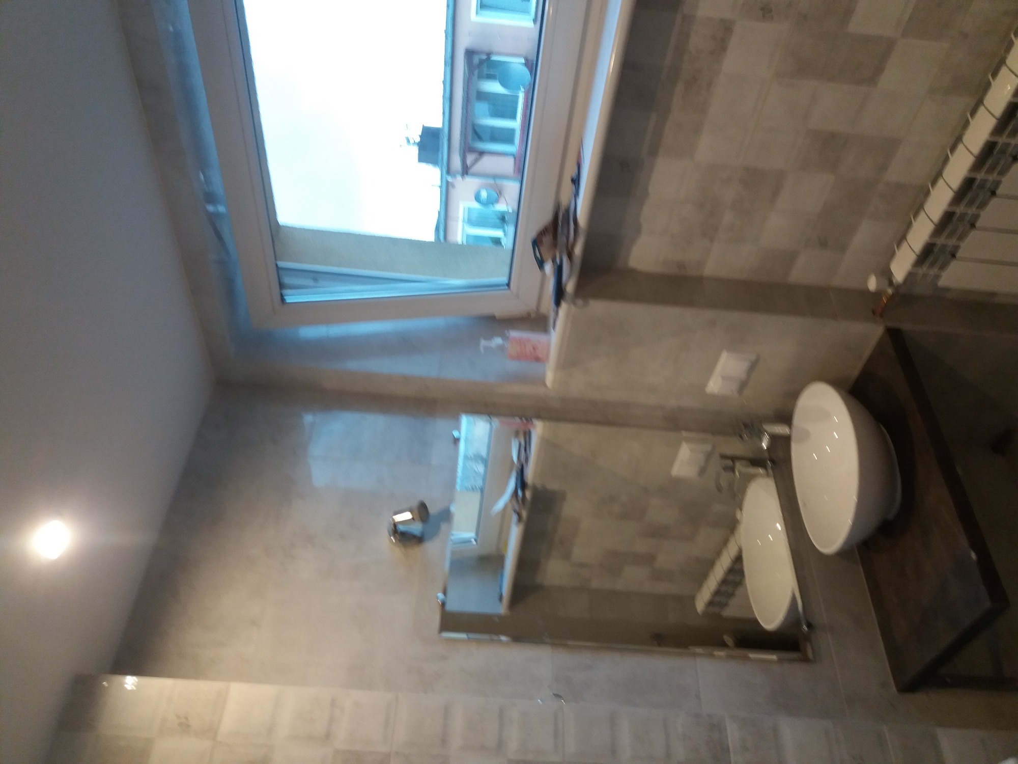 Nowoczesna łazienka w szarych odcieniach z umywalką nablatową i dużym lustrem, widok na zewnątrz przez okno dachowe.