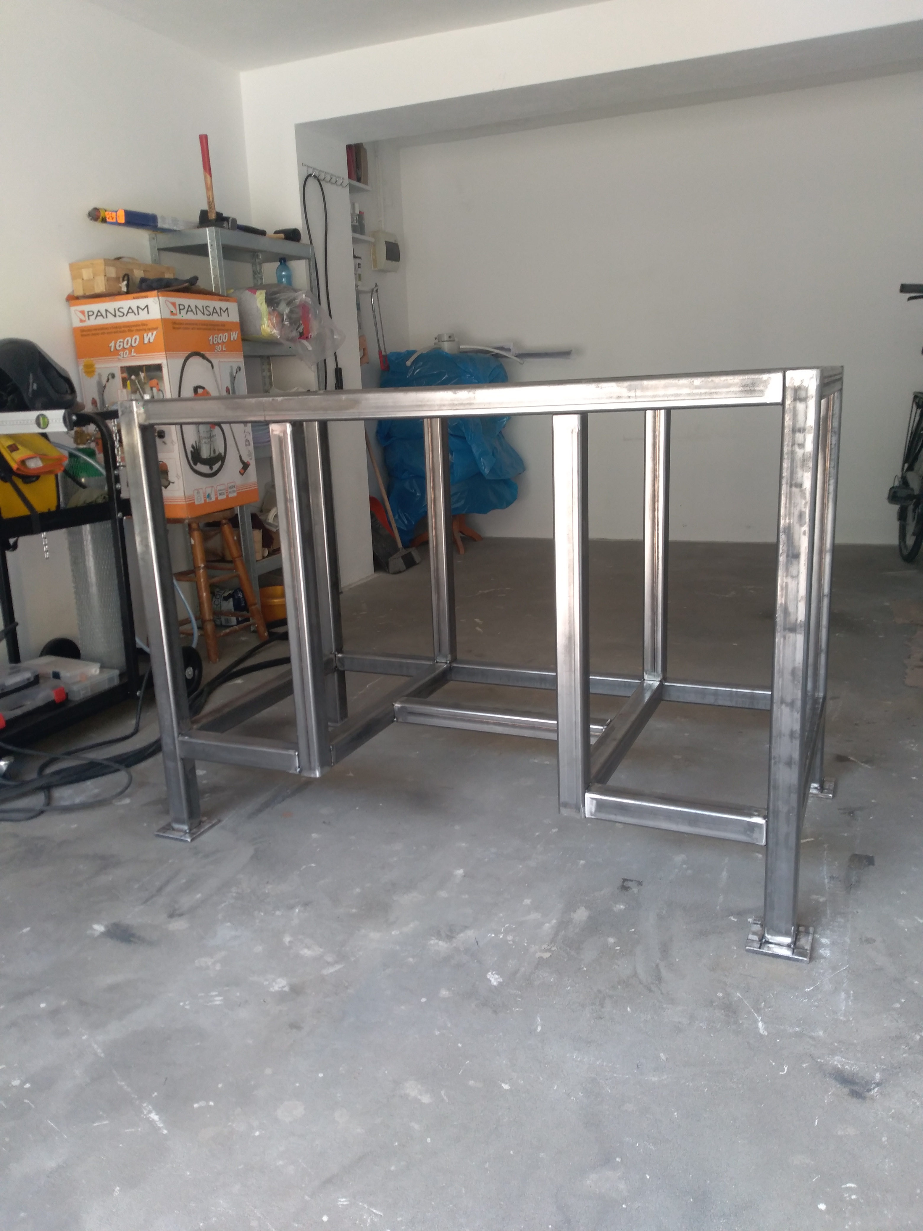 Metalowa konstrukcja stołu z profili kwadratowych, spawana, surowa, w garażu, widoczne spawy.