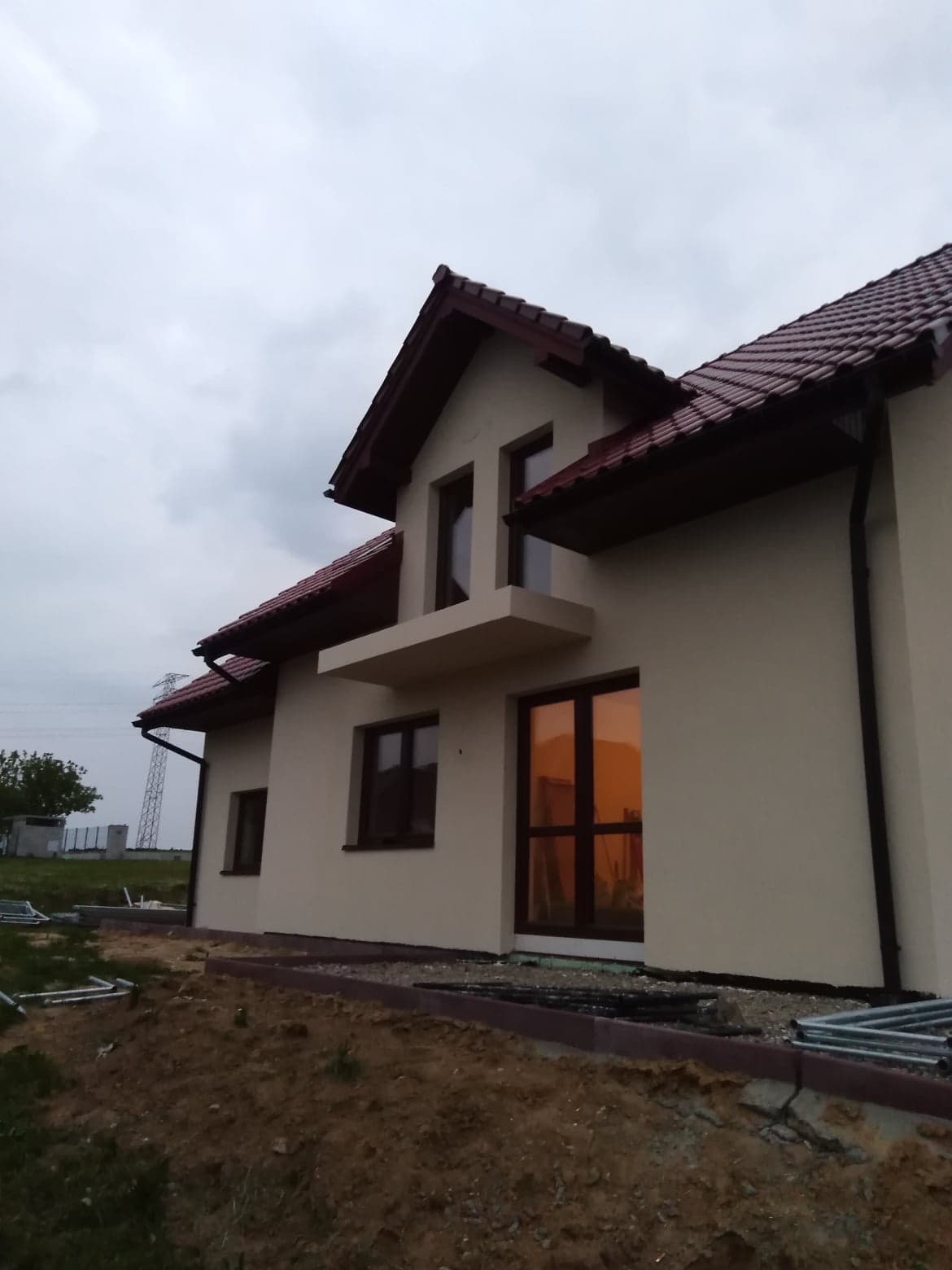 Nowo otynkowany dom jednorodzinny z czerwonym dachem i widocznymi elementami przygotowania terenu pod ogród.