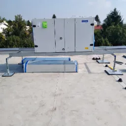 Centrala wentylacyjna Komfovent Verso zamontowana na dachu budynku komercyjnego, widoczne elementy montażowe i przewody wentylacyjne w folii.