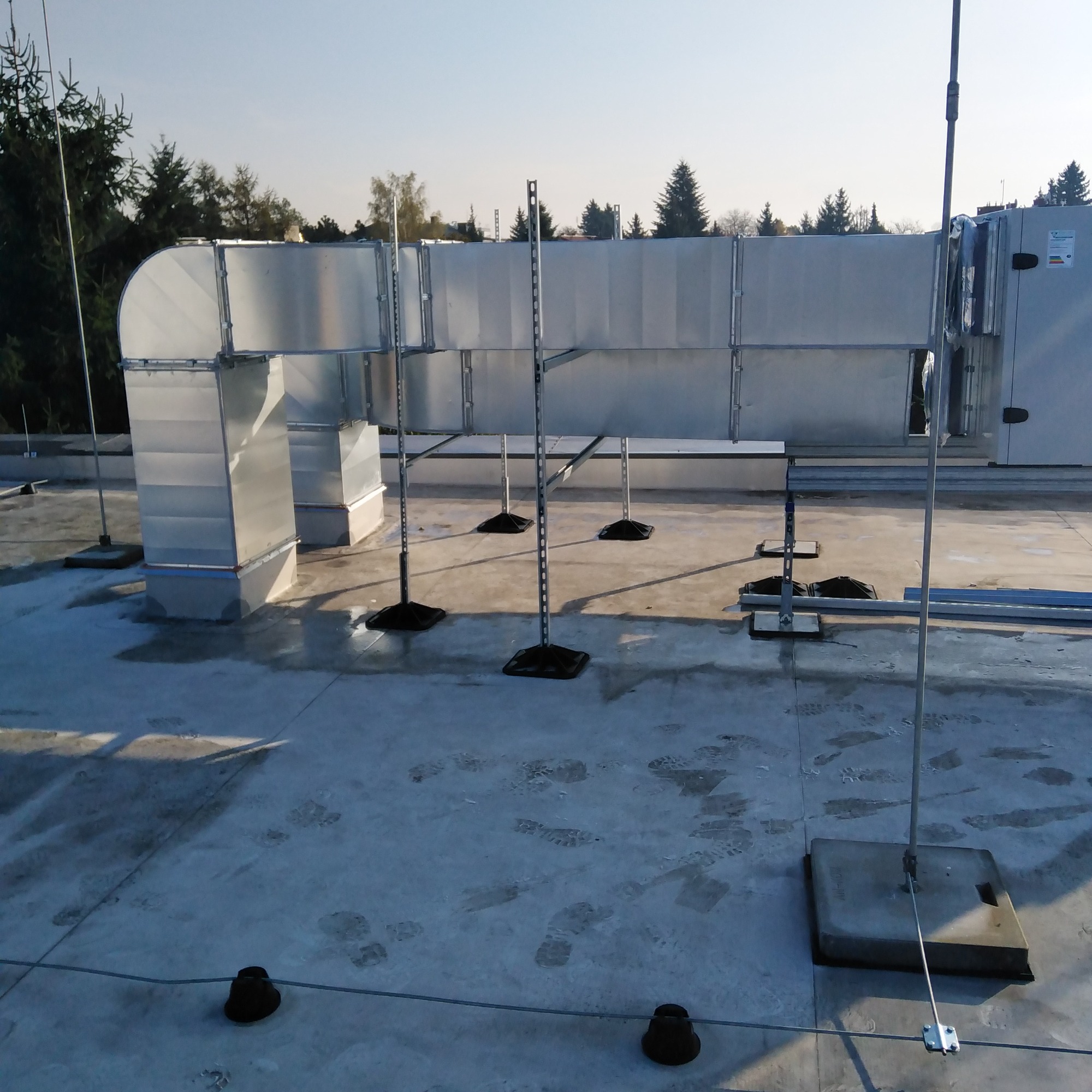 System kanałów wentylacyjnych z ocynkowanej blachy na dachu budynku, widoczne podpory i odgromniki, ślady na dachu.