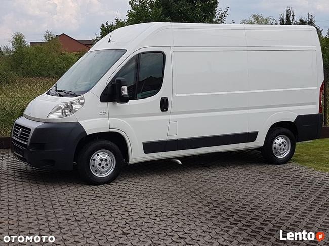 Biały furgon dostawczy Fiat Ducato sfotografowany z boku na tle zieleni.