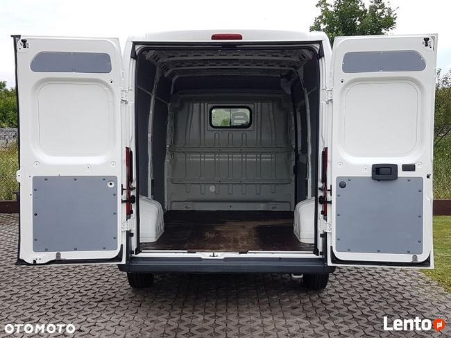 Wnętrze pustego, białego busa dostawczego z otwartymi tylnymi drzwiami, widok od tyłu, na podłodze widoczne ślady użytkowania.