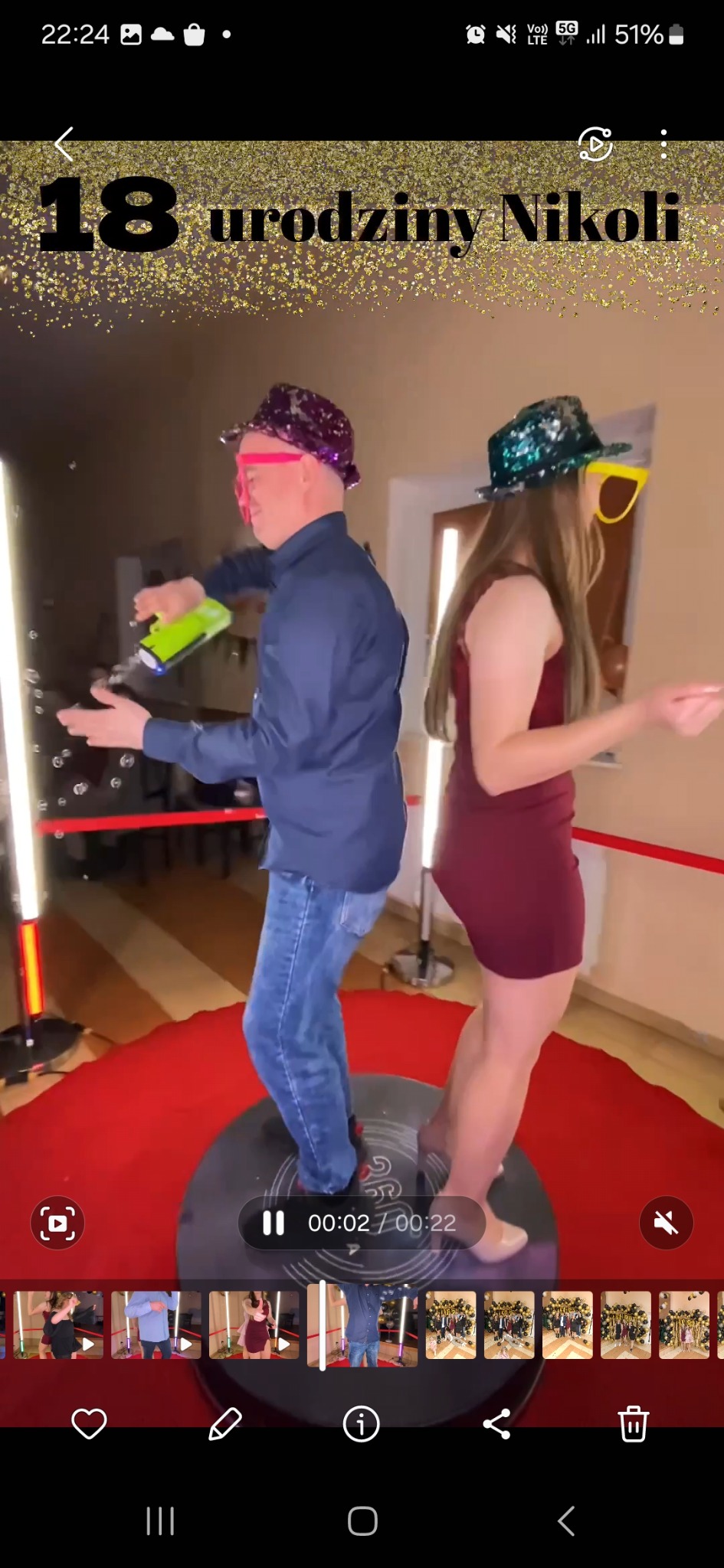 Dwie osoby w zabawnych okularach i kapeluszach pozują na platformie z czerwonym dywanem, otoczonej lampami, podczas 18 urodzin.