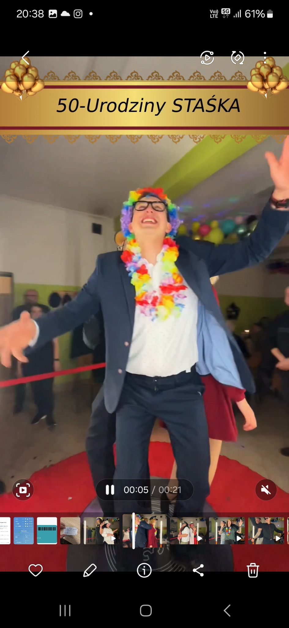 Radosny mężczyzna w przebraniu na 50. urodzinach Staszka, z kolorowym wieńcem i peruką, tańczy na czerwonym dywanie podczas imprezy.