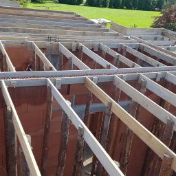 Fectumpro - Wznoszenie ścian domu z pustaków ceramicznych, widoczne drewniane podpory stropu i szalunki obwodowe, w tle zielony trawnik.