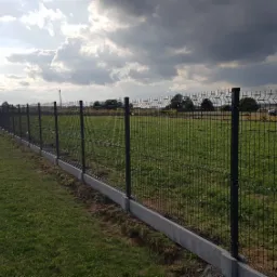 Długi, panelowy płot z podmur&oacute;wką z betonu, otaczający teren zielony w Choczni, widziany w pochmurny dzień.