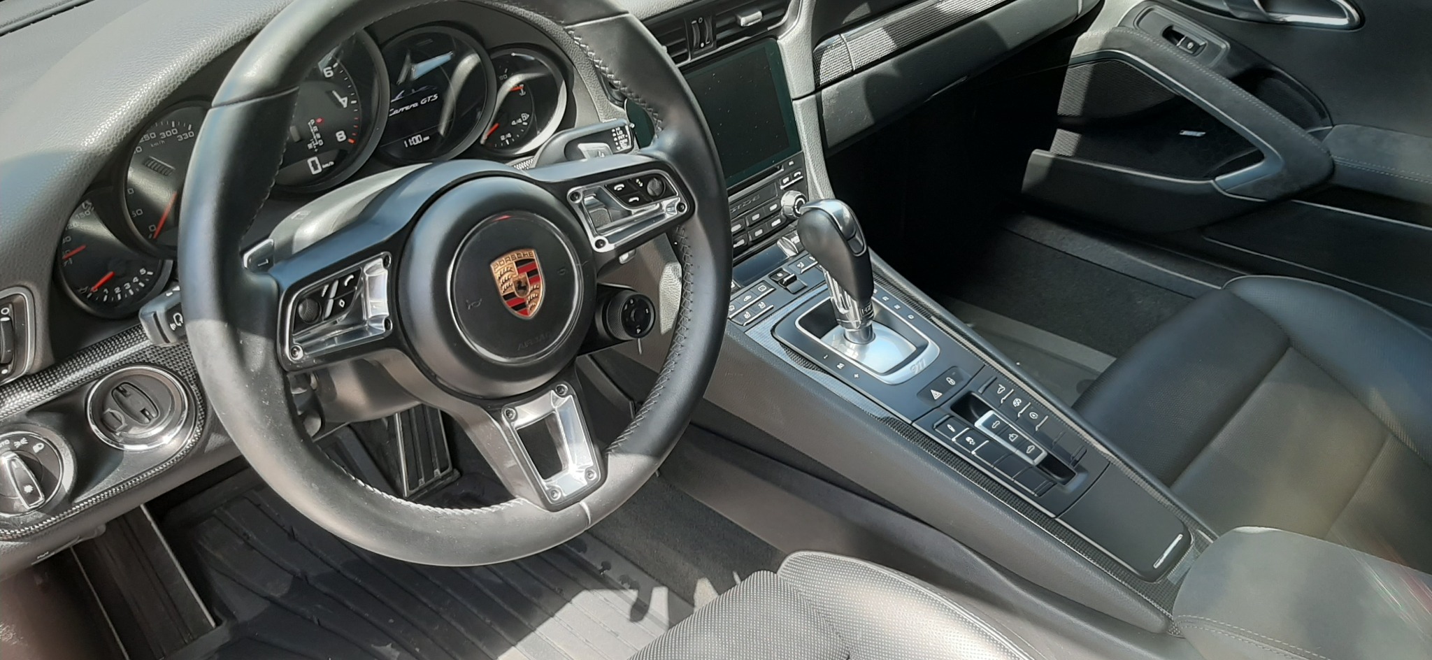 Wnętrze samochodu Porsche Carrera GTS z widoczną deską rozdzielczą, kierownicą z logo Porsche i dźwignią zmiany biegów.