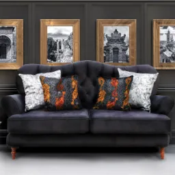 Ciemnoszara sofa z pikowanym oparciem i poduszkami w geometryczne wzory i tygrysy, na ścianie cztery obrazy w złotych ramach, obok stolik z dekoracyjnym czaszką i świecami.