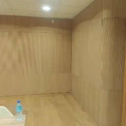 Drewniana boazeria ścienna z pionowymi żłobieniami, zaokrąglony narożnik, drewniana podłoga i drzwi, butelka wody na stole.