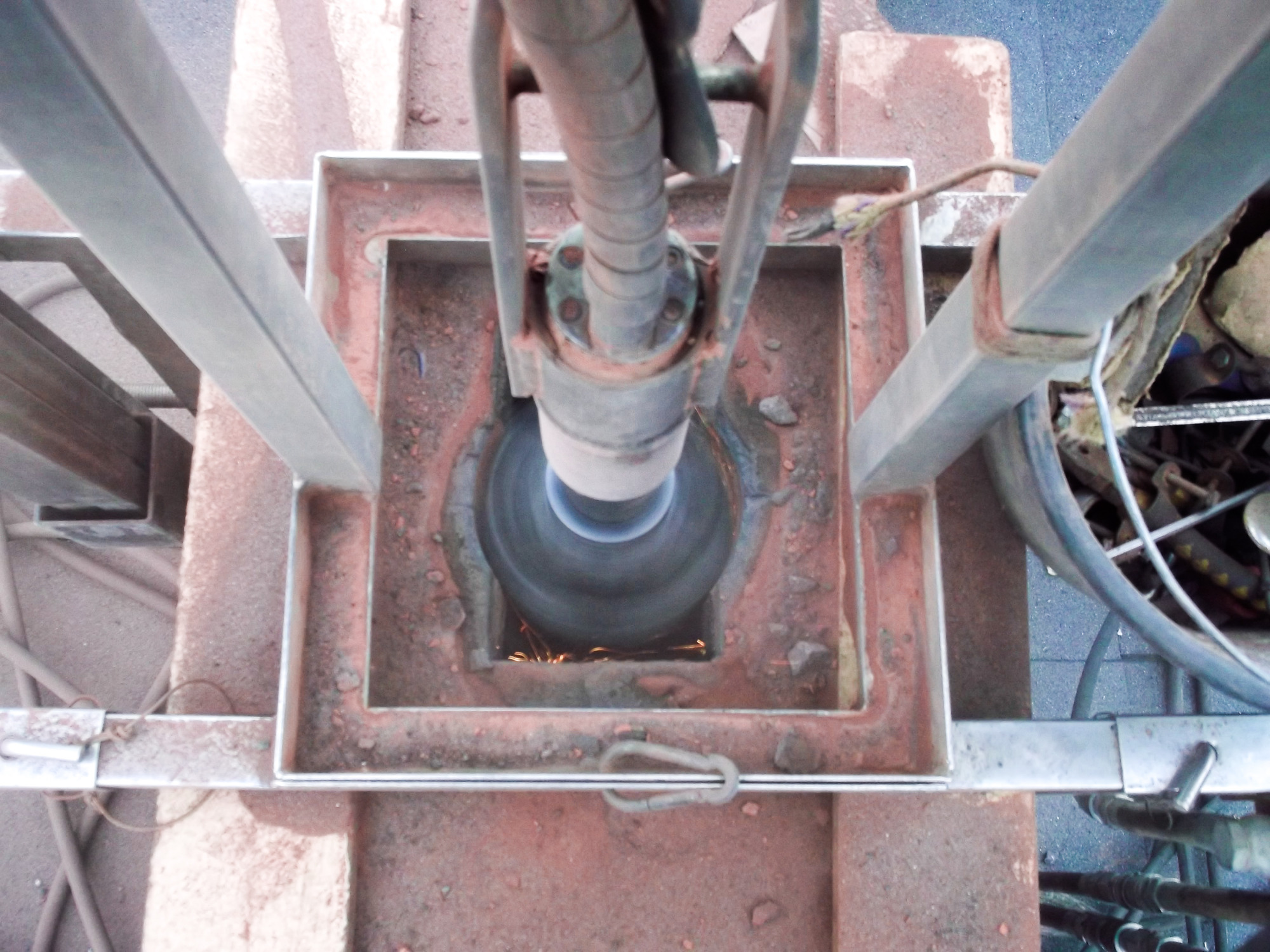 Widok z góry na proces frezowania komina z iskrzeniem, z metalową konstrukcją wsporczą i narzędziami w tle.