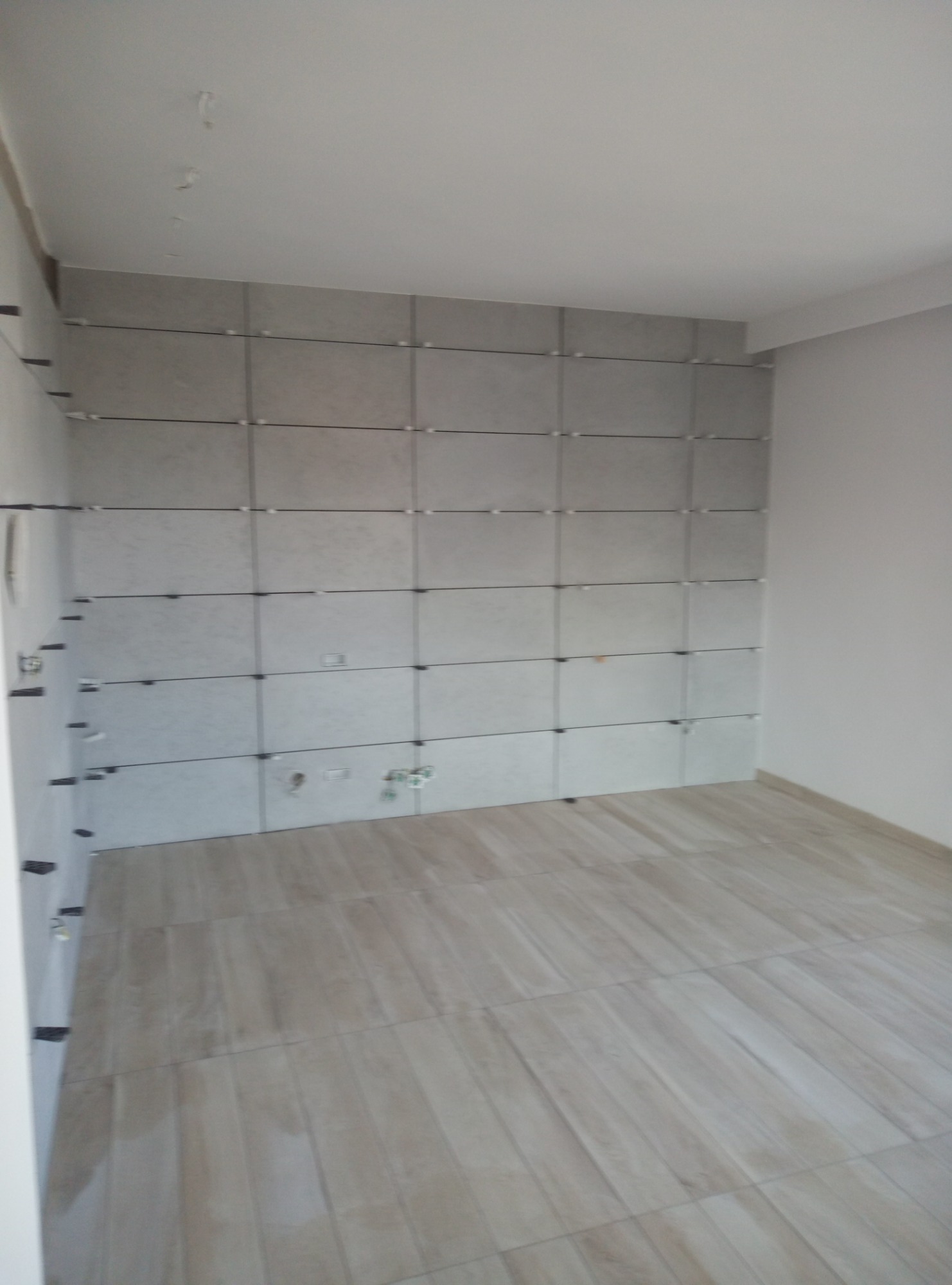 Płytki ceramiczne na ścianie i podłodze w trakcie montażu, z widocznymi krzyżykami dystansowymi, jasne wnętrze łazienki w stanie surowym.