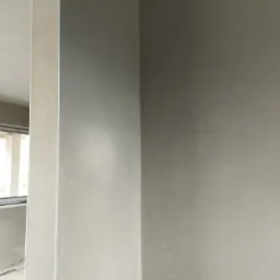 Świeżo położony, gładki tynk w jasnym odcieniu szarości na ścianie wewnętrznej, widoczne wystające przewody elektryczne przy suficie.