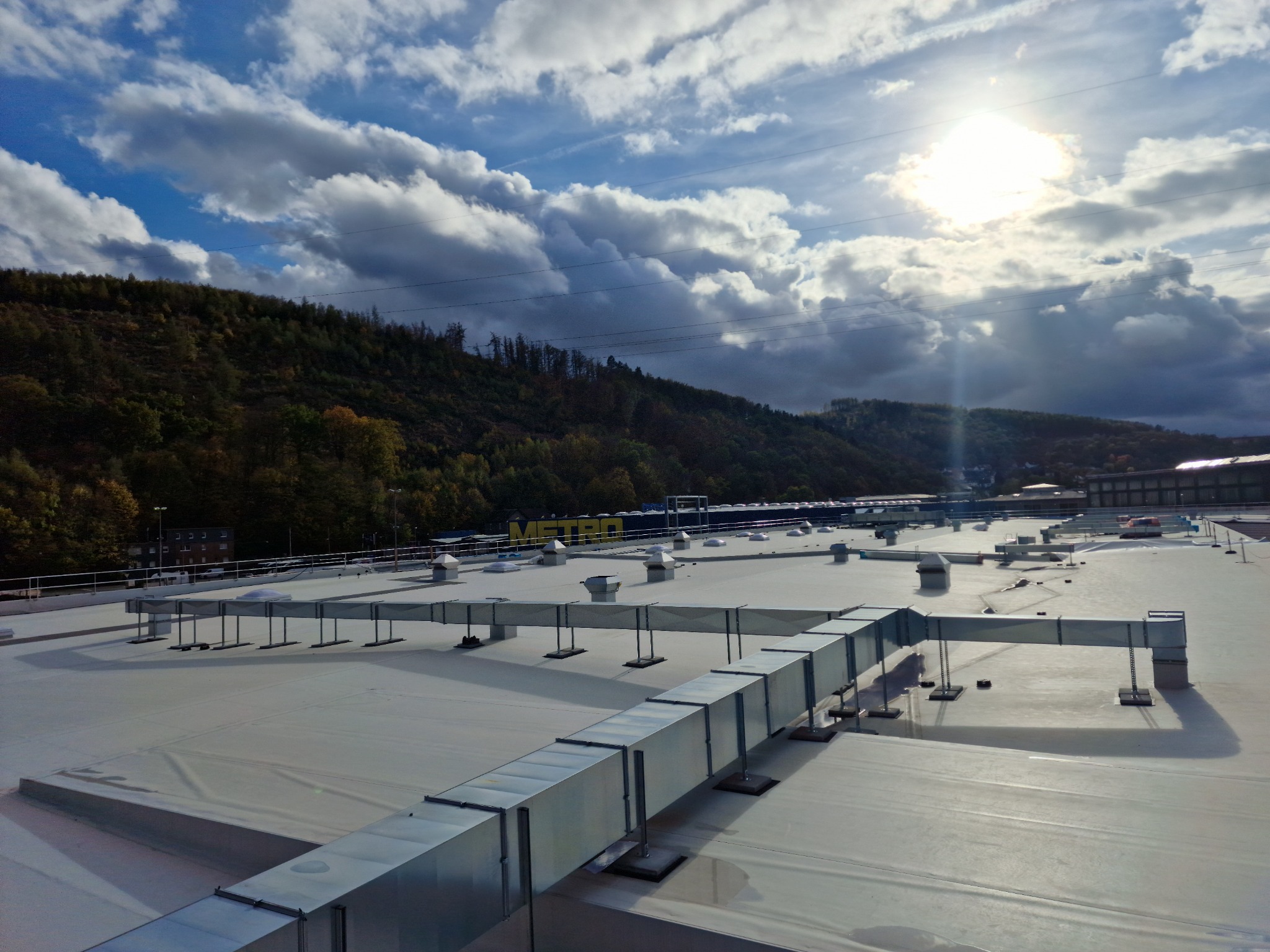 System wentylacji kanałowej na płaskim dachu budynku komercyjnego, widok z góry na tle pochmurnego nieba i zalesionych wzgórz.