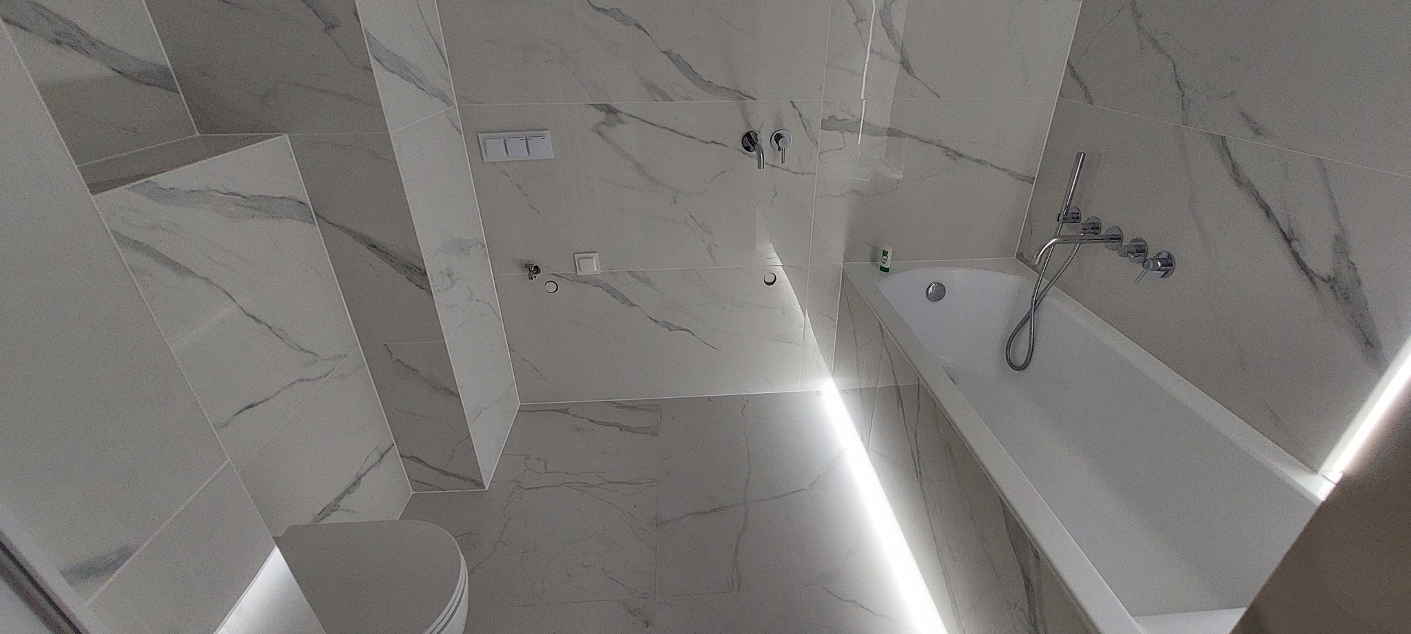 Biała łazienka z marmurowymi płytkami, armaturą chromowaną i podświetleniem LED wzdłuż wanny.