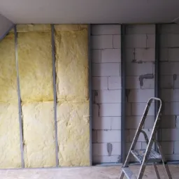 Wnętrze w trakcie prac remontowych: ocieplona wełną mineralną ściana z metalowym stelażem, fragment ściany z bloczków betonowych, drabina aluminiowa, surowy sufit z płyt gipsowych i podłoga z płyty...