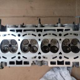 DB Service Dariusz Bryl - Głowica silnika samochodowego z widocznymi zaworami, leżąca na kartonowym podłożu, widok z góry.