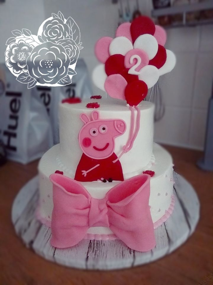 Dwupoziomowy tort urodzinowy z dekoracjami z lukru plastycznego: różowa świnka Peppa trzymająca baloniki z cyfrą 2, ozdobiony dużym różowym kokardą i drobnymi elementami dekoracyjnymi.