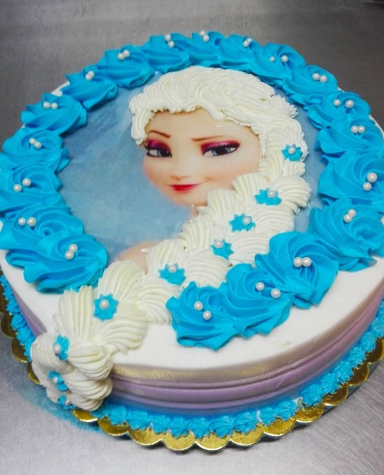Tort urodzinowy z wizerunkiem postaci z bajki 'Kraina Lodu', dekorowany kremem w odcieniach bieli i błękitu, z delikatnymi perłowymi koralikami.
