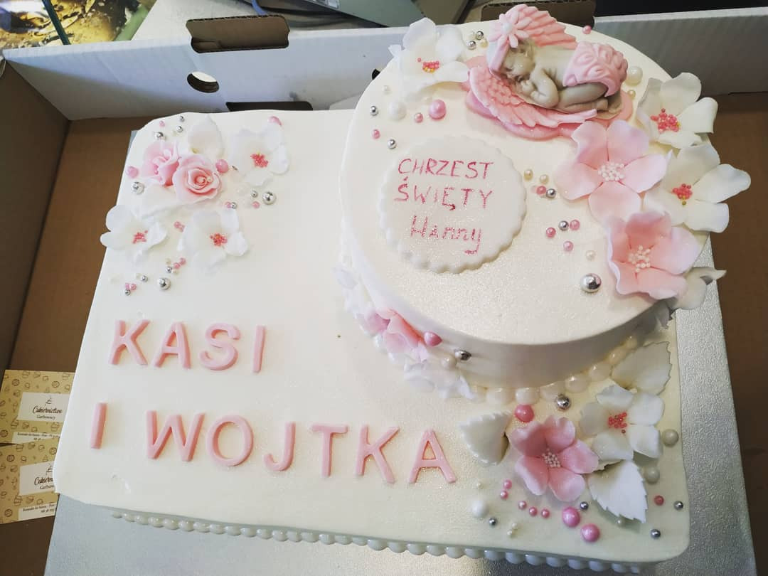 Dwupoziomowy tort na Chrzest Święty Hanny, z imionami Kasi i Wojtka, ozdobiony kwiatami i figurką śpiącego dziecka, wykonany w cukierni w Świebodzinie.