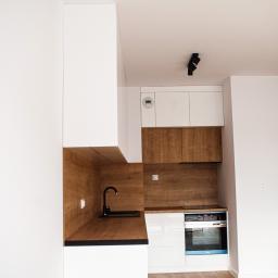 Kuchnia bez uchwytowa w stylu loftowym. Meble wykonane z płyty meblowej w białym połysku. Wykończenie drewnem dąb nagano, czarny mat. Zabudowana pralka, lodówka, zmywarka, okap. Szafki bez uchwytowe otwierane systemem push-open. 