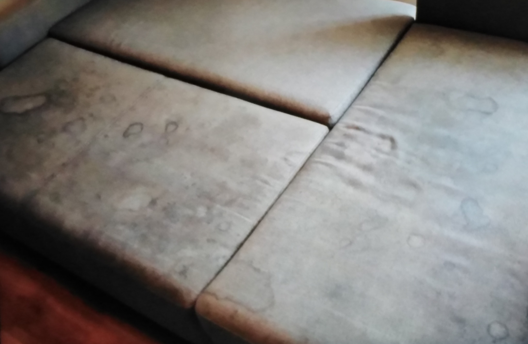 Brudna, jasna kanapa z widocznymi plamami na każdym segmencie siedziska.