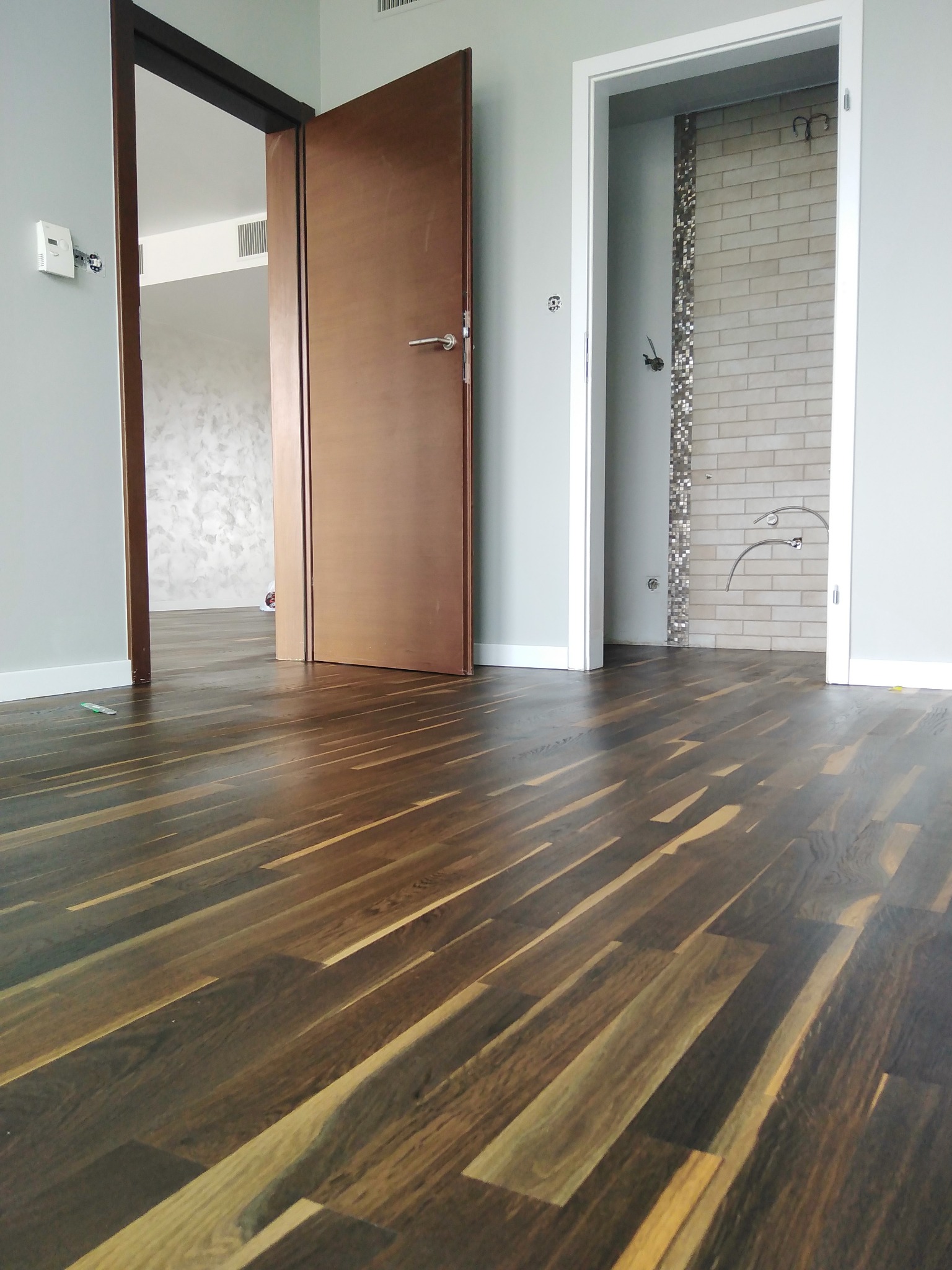 Wypolerowana, ciemna drewniana podłoga w nowym wnętrzu z otwartymi drzwiami do łazienki i pokoju z dekoracyjną ścianą.