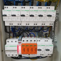 Rozdzielnica elektryczna z zamontowanymi bezpiecznikami Schneider, ogranicznikiem przepięć Relpol i modułami SIMTEC, widoczne okablowanie.