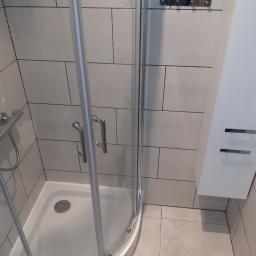 Remonty - Kabina prysznicowa z białymi płytkami imitującymi cegłę, chromowaną armaturą i białą szafką wiszącą z dwoma uchwytami.