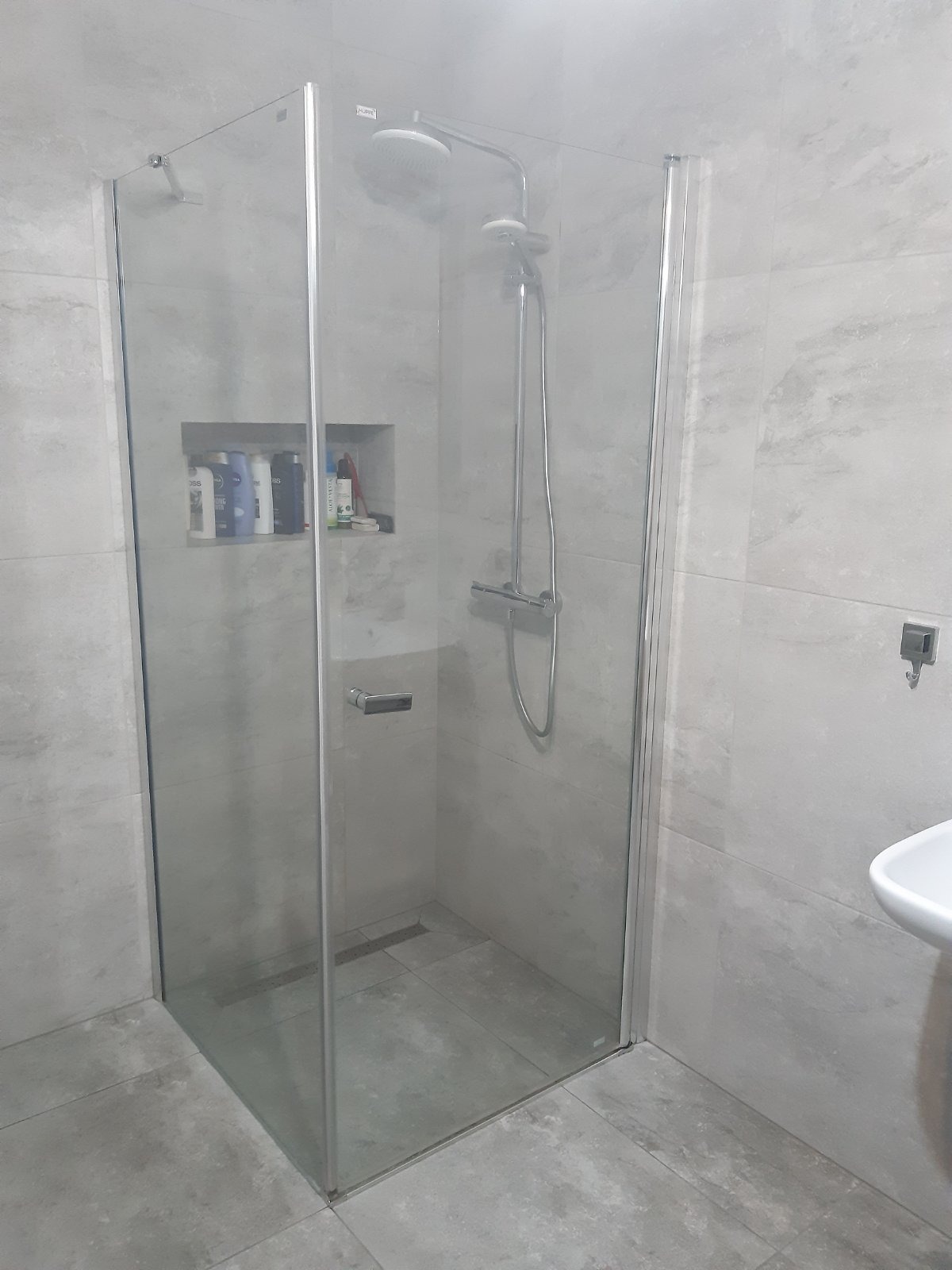 Szklana kabina prysznicowa z deszczownicą i wnęką na kosmetyki, wykończona szarymi płytkami w łazience we Wrocławiu.