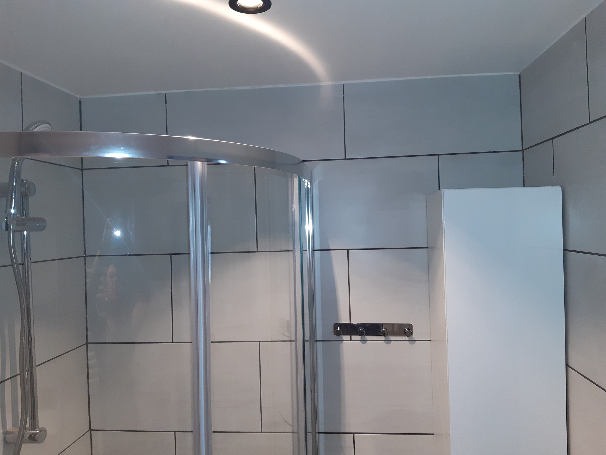 Nowoczesna kabina prysznicowa z chromowanymi elementami i szarymi płytkami w łazience, oświetlenie punktowe w suficie.