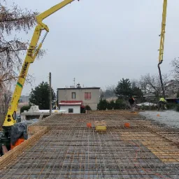 Zalewanie stropu monolitycznego z użyciem pompy do betonu Schwing S-34, widoczna siatka zbrojeniowa i dwóch pracowników w tle.