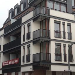 Przedsiębiorstwo Produkcyjno Handlowe MIRAMET Jerzy Kwiatkowski - Nowoczesny budynek mieszkalny w Bydgoszczy z balkonami z czarnymi, metalowymi balustradami, wykonanymi według projektu dewelopera. Widoczny baner reklamowy apartamentów na jednym z balkonów.