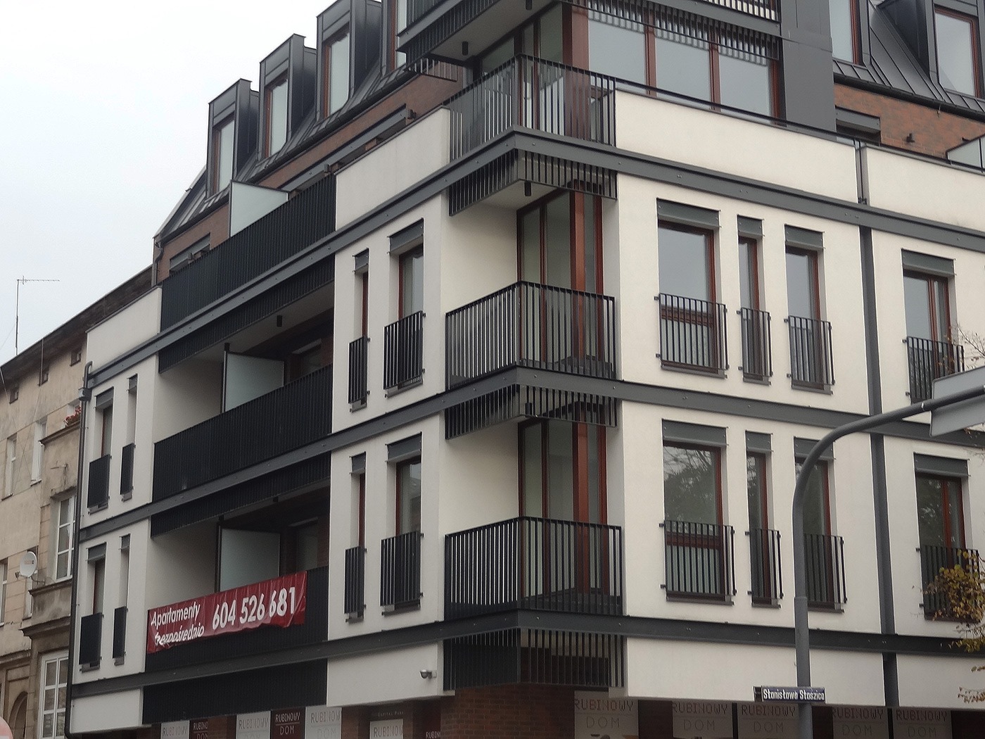 Nowoczesny budynek mieszkalny w Bydgoszczy z balkonami z czarnymi, metalowymi balustradami, wykonanymi według projektu dewelopera. Widoczny baner reklamowy apartamentów na jednym z balkonów.