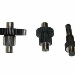 Trzy metalowe przekładnie zębate o różnych rozmiarach i konfiguracjach, ułożone na białym tle. Jedna przekładnia leży poziomo, dwie stoją pionowo. Widoczne ślady obróbki.