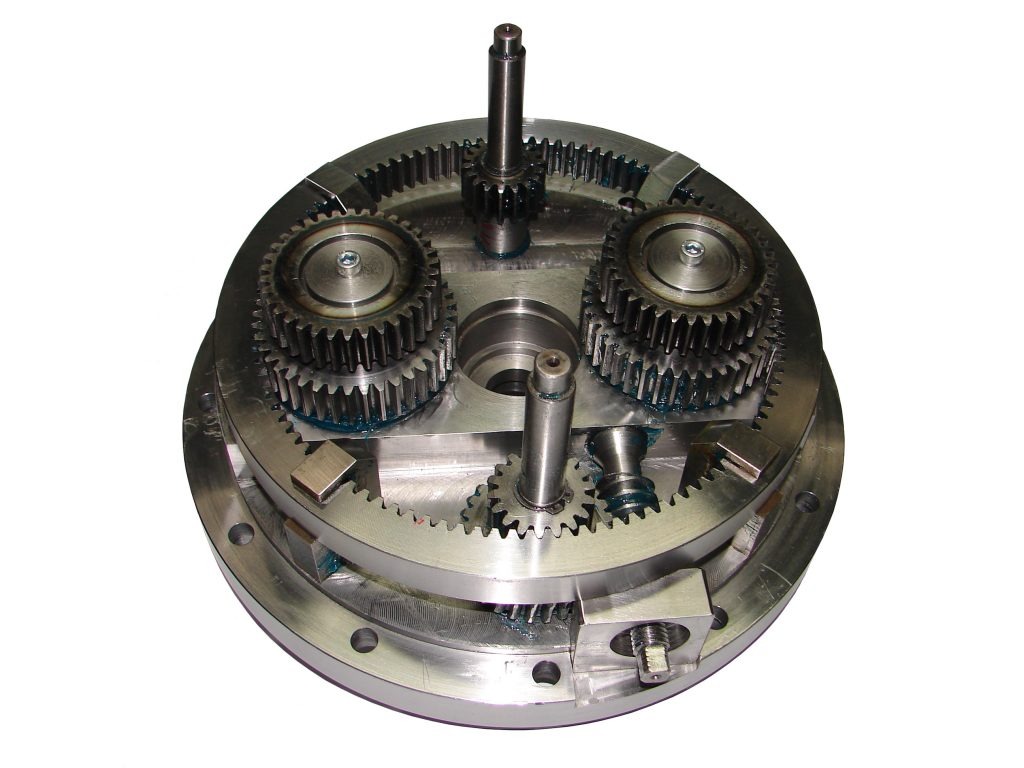 Metalowa przekładnia planetarna z widocznymi kołami zębatymi i śladami smaru, sfotografowana z góry na białym tle.