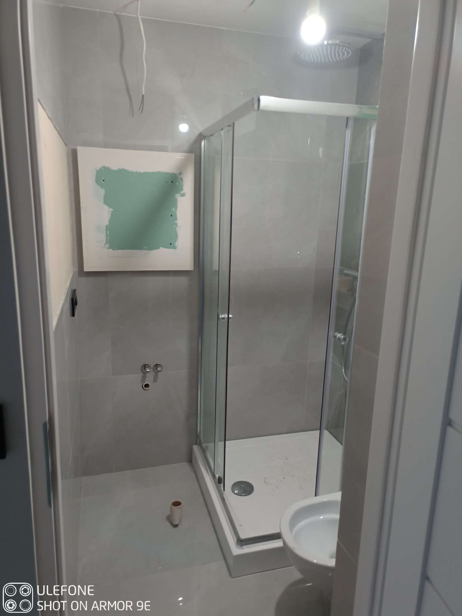 Łazienka w trakcie remontu w Skawinie: widoczna kabina prysznicowa, częściowo położone szare płytki, przygotowana ściana z płyt karton-gips, wystające kable.